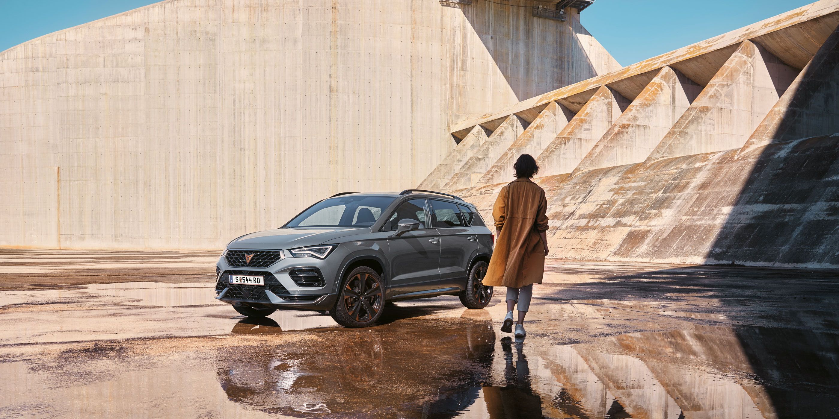 Eine Person geht auf einen CUPRA Ateca zu, der die markanten, athletischen Linien und die dynamische Form zeigt, die den Geist der CUPRA Tribe verkörpern.