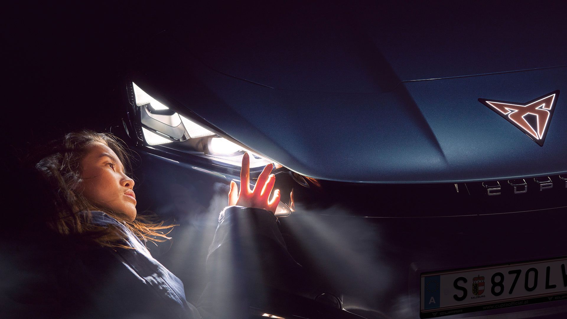 Detailaufnahme des Matrix LED Scheinwerfer eines CUPRA Tavascan, eine Frau befindet sich neben dem Auto.