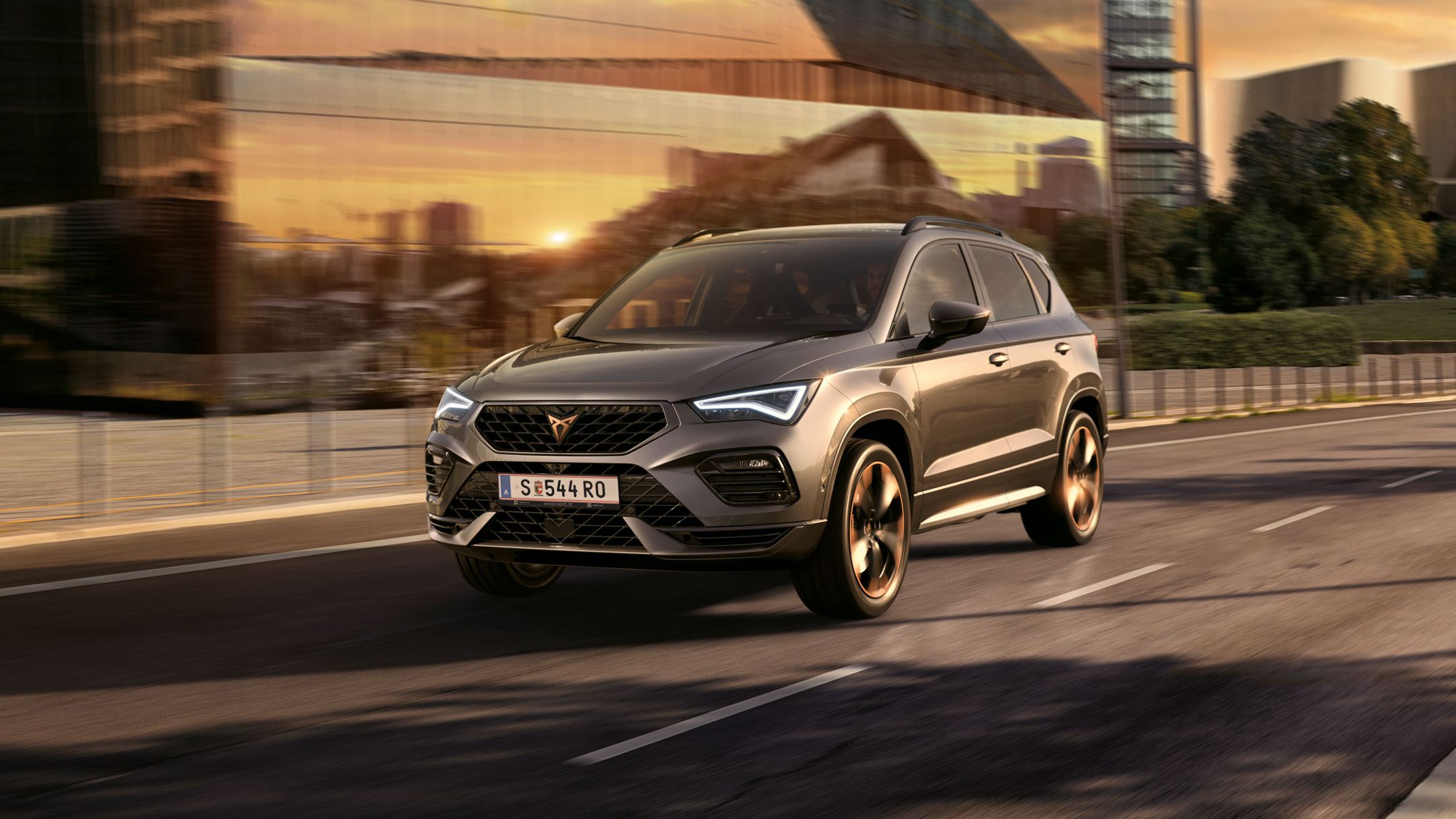 Ein Cupra Ateca fährt auf einer Straße. Im Hintergrund ist ein modernes Gebäude abgebildet.